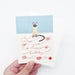 Hand holding a birthday card with a cat illustration and 'Happy Birthday' text on a light blue background.